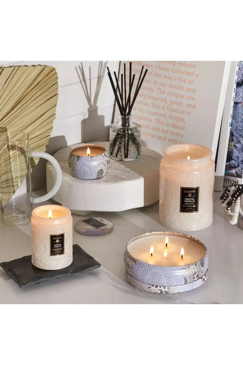 Et hvitt, teksturert lys i en dekorativ glasskrukke med et svart etikett.